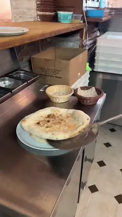 Dos focaccias doradas, con la superficie ampollada, cayendo sobre un plato en la encimera de acero.