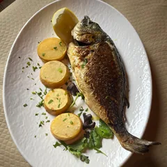 Un pescado entero visto desde arriba, con la piel dorada y tostada, sobre un plato blanco.